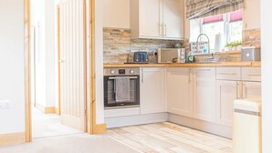 A modern kitchen with white cabinets, a built-in oven, a microwave, and a toaster. - 1 bedroom accommodation in Ulverston (Ulverston)