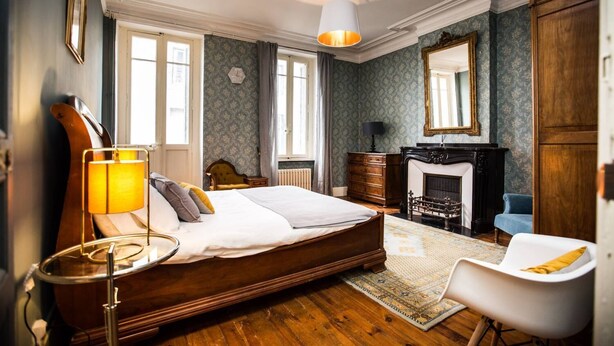 Un dormitorio con una cama grande, un aparador de madera, una silla, una chimenea y un espejo.