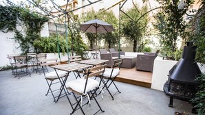 Un patio al aire libre con mesa y sillas de madera, una parrilla y un área de estar con cojines.