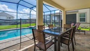 A covered patio with a glass table and chairs, a pool, and a view of a residential area.