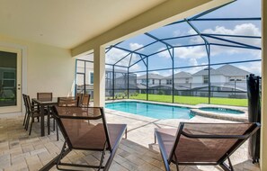 Un patio cubierto con piscina, mobiliario exterior y vistas a una zona residencial.