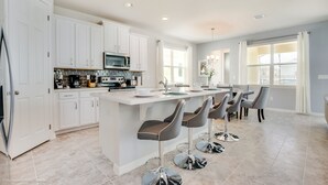 A modern kitchen with white cabinets, a central island with bar stools, a microwave, and a dining area with chairs.