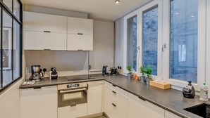 A modern kitchen with built-in appliances, a window with a view, and a countertop with a coffee maker and toaster. - Madeleine- Charming, quiet, upscale apartment - 2 bedrooms 6 people (Paris)