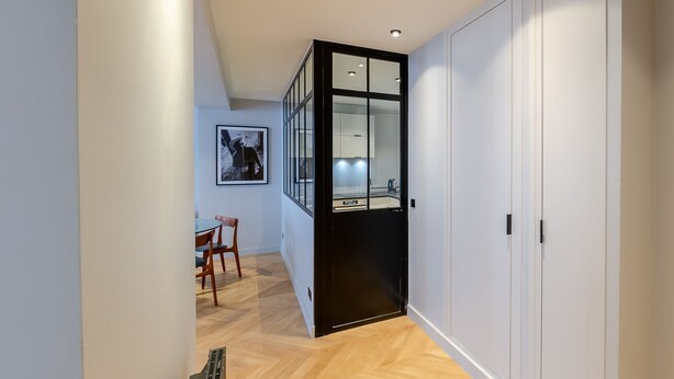 A hallway with a dining area, a black-framed glass door, and white cabinets. - Madeleine- Charming, quiet, upscale apartment - 2 bedrooms 6 people (Paris)