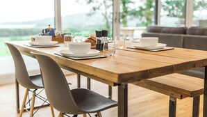 Una mesa de comedor con sillas, vistas a zonas verdes y un sofá al fondo.