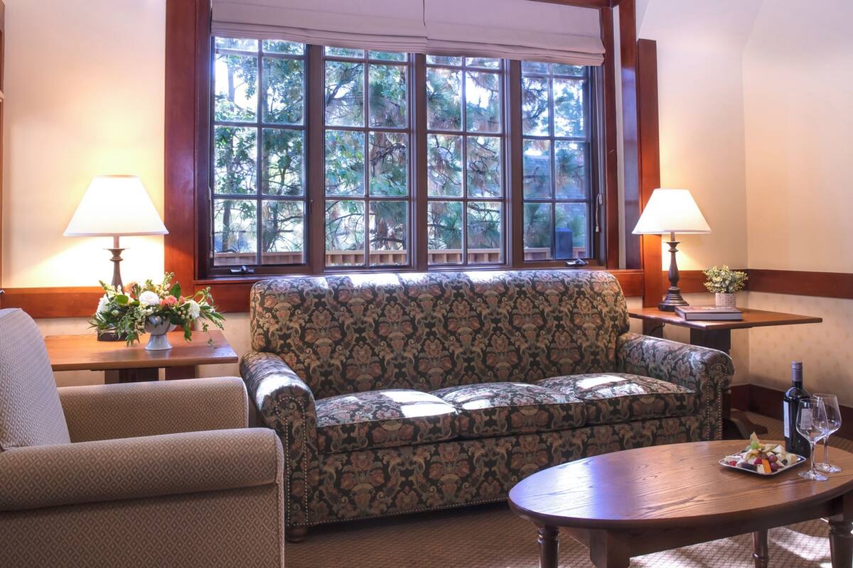 Una sala de estar con un sofá estampado, dos sillones, una mesita de centro y un ventanal con vista a árboles.