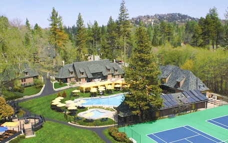 A resort with multiple buildings, a swimming pool, tennis courts, and a forested backdrop.