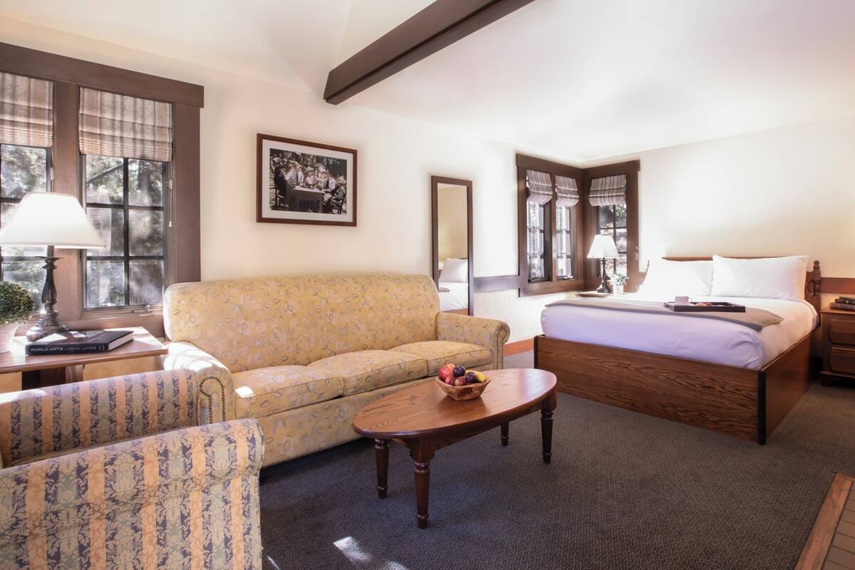 Una habitación de hotel con una cama, un sofá, una mesita con fruta y una lámpara.