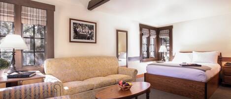 A hotel room with a bed, a sofa, a small table with fruit, and a lamp.