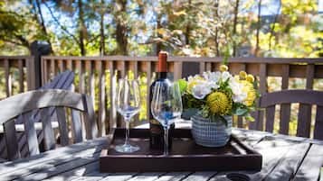 A wooden table with a tray holding a wine bottle, two glasses, and a vase of flowers.