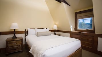 A bedroom with a large bed, two bedside tables with lamps, a window with a view, and wooden paneling.