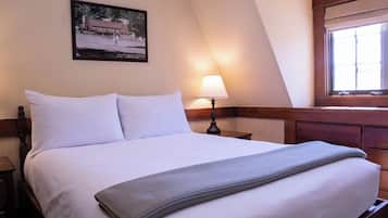 A neatly made bed with white linens, a single bedside table with a lamp, and a framed picture on the wall.