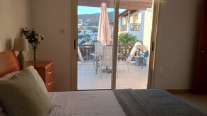 A bedroom with a bed, a nightstand with a lamp, and a view of an outdoor patio with a table, chairs, and an umbrella. - Fantastic Sea View Apartment With Large Balcony (Paphos)