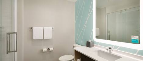 Un baño moderno con cabina de ducha de vidrio, inodoro blanco, lavamanos con espejo y toallero.