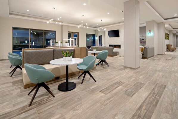 Eine moderne Lounge-Ecke mit Sitzgelegenheiten, einem runden Tisch und einem an der Wand befestigten Flachbildfernseher.