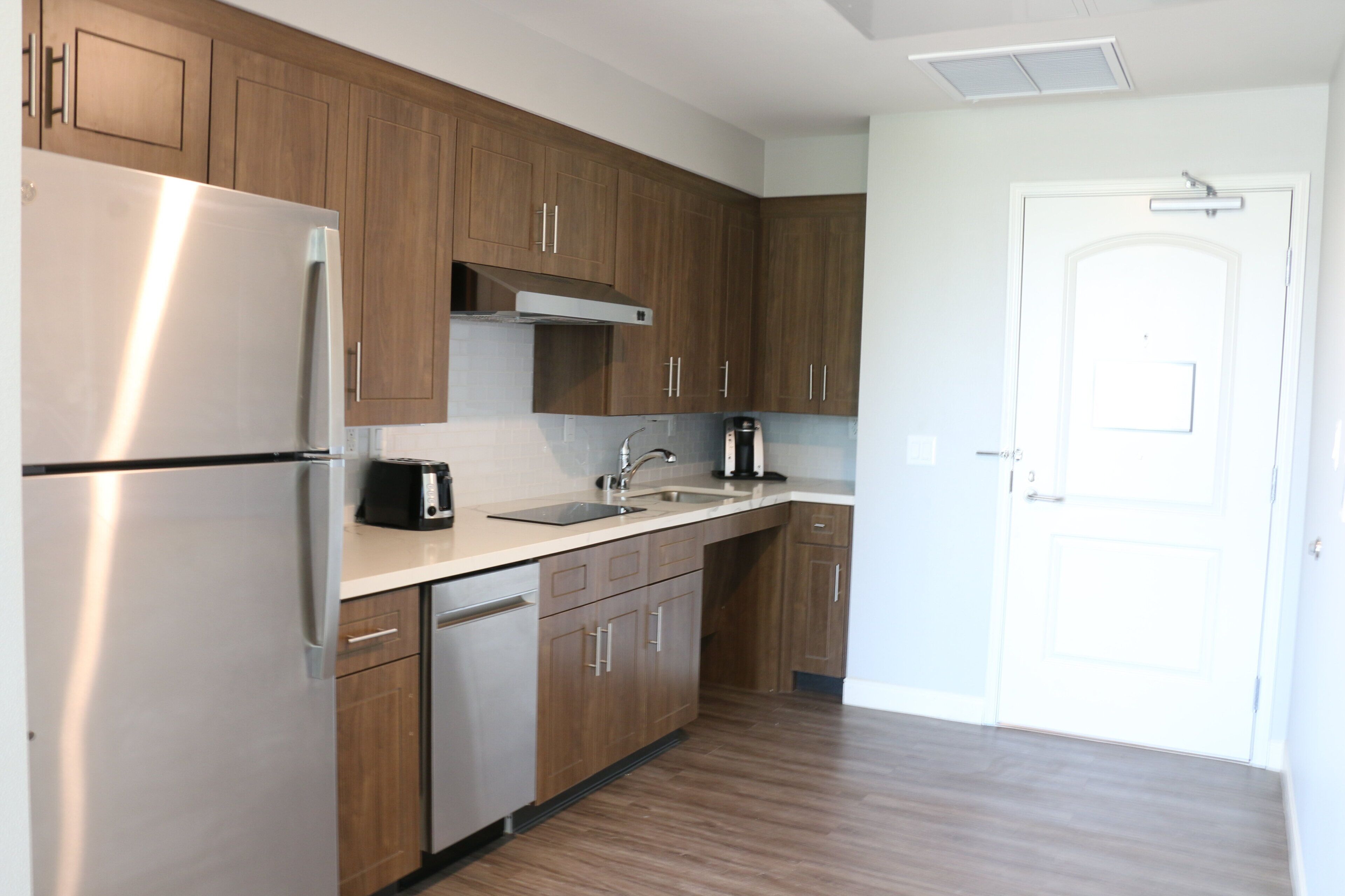 Una cocina moderna con electrodomésticos de acero inoxidable, armarios de madera y encimera blanca.