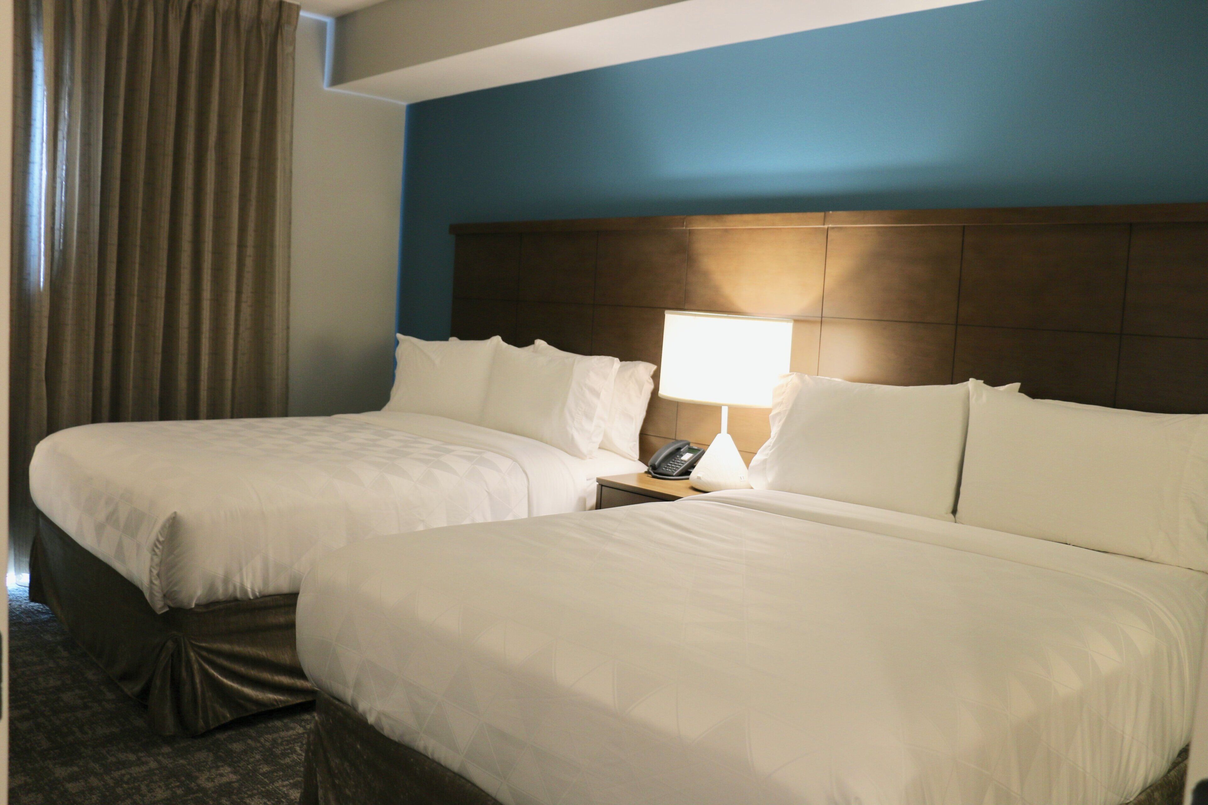 A hotel room with two beds, a nightstand with a lamp, and a telephone.