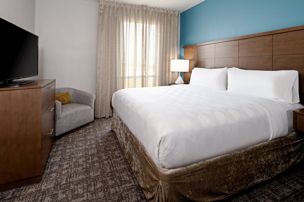 Ein Hotelzimmer mit einem großen Bett, einem Fernseher, einem Schreibtisch mit Stuhl und einem fensterbepflanzten Fenster.