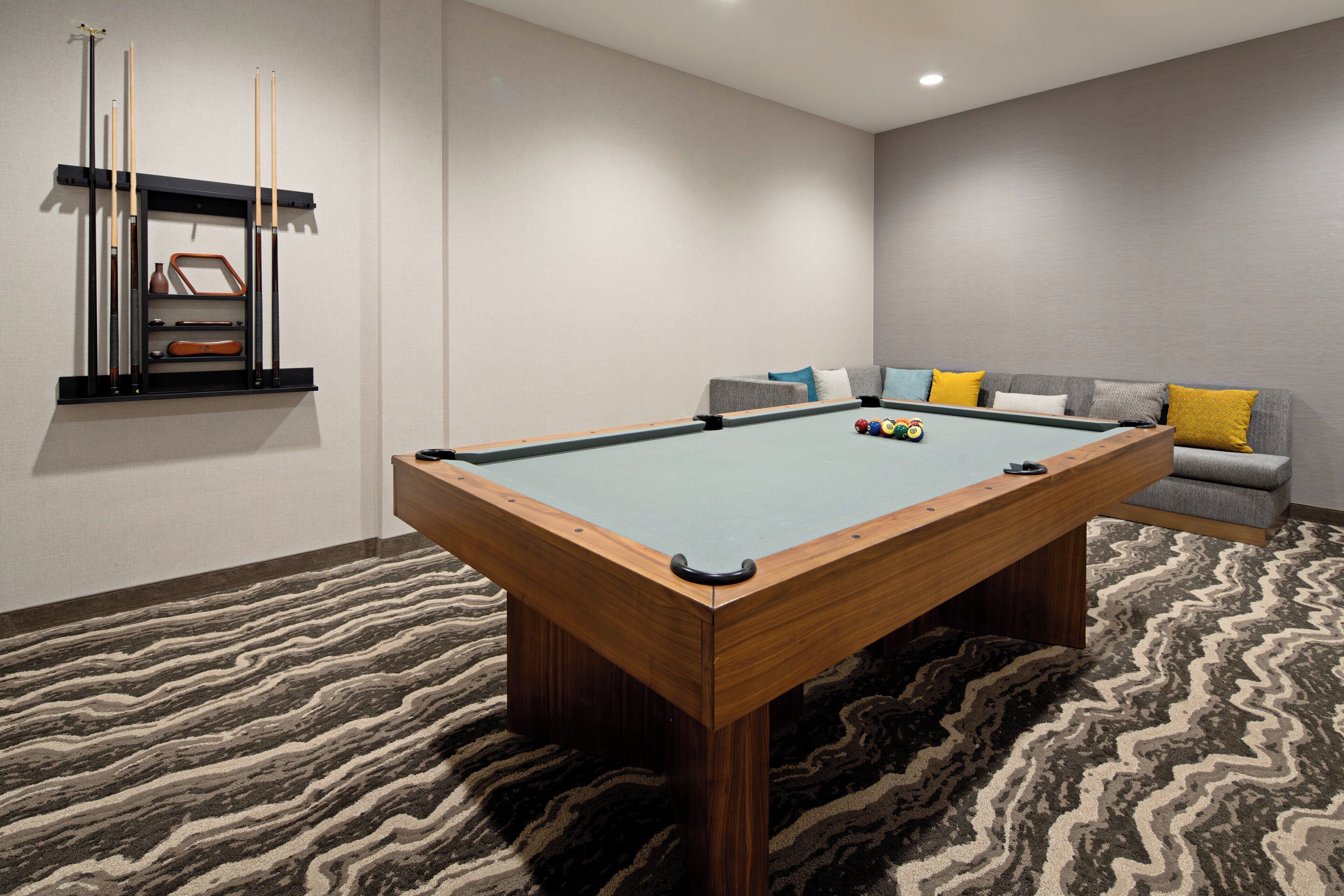 Une table de billard recouverte d’un tapis à rayures, un canapé avec des coussins et un porte-queue fixé au mur.