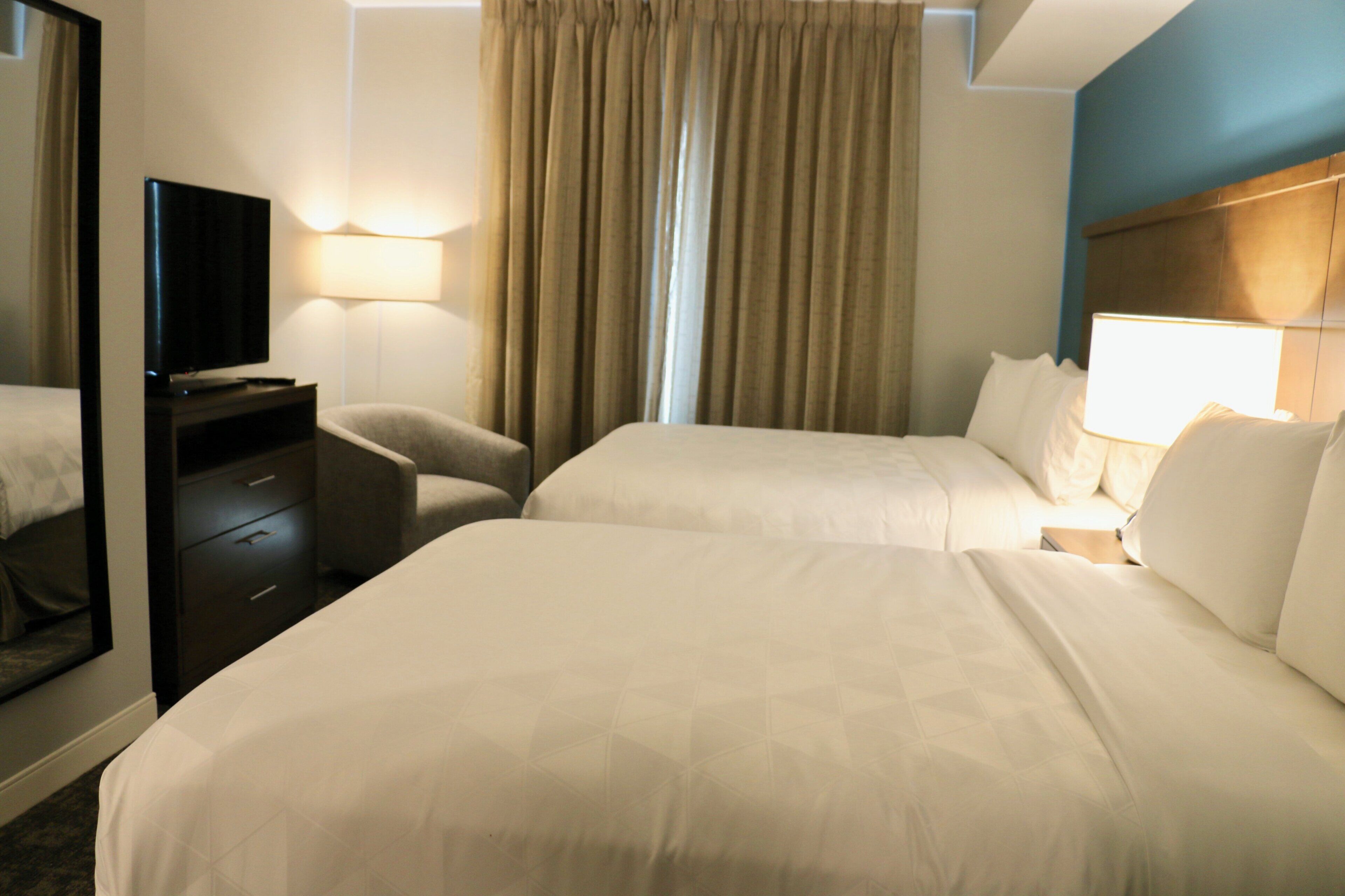 A hotel room with two beds, a desk, a chair, a television, and a window with curtains.