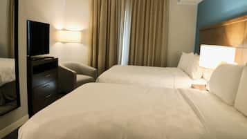 A hotel room with two beds, a desk, a chair, a television, and a window with curtains.