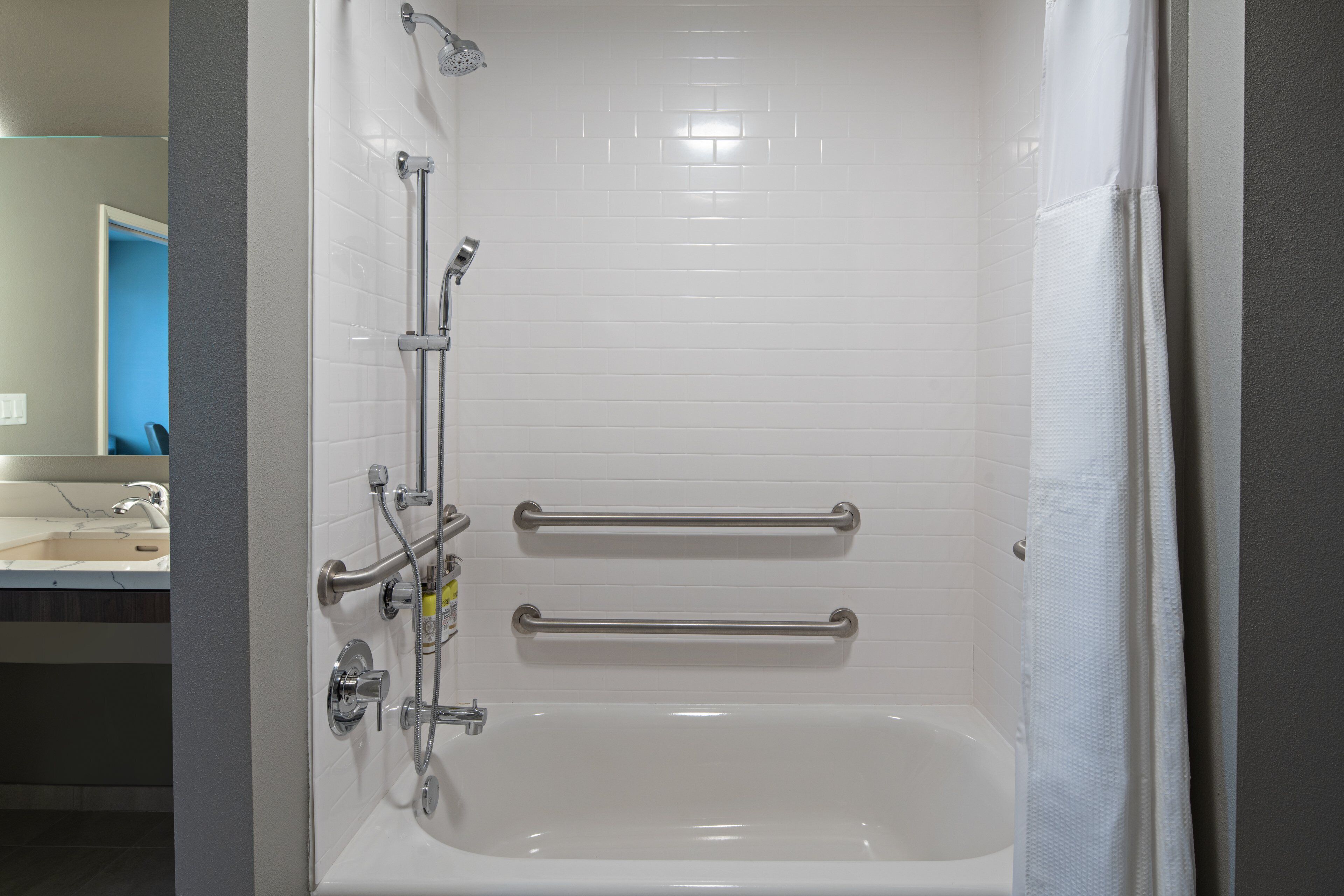 Une salle de bain moderne avec une baignoire blanche, des barres d’appui et une pomme de douche.
