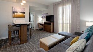 A hotel room with a sofa, a desk with a chair, a TV, and a painting on the wall.