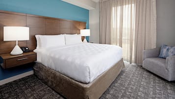 A hotel room with a large bed, two bedside tables with lamps, a grey sofa, and a window with curtains.