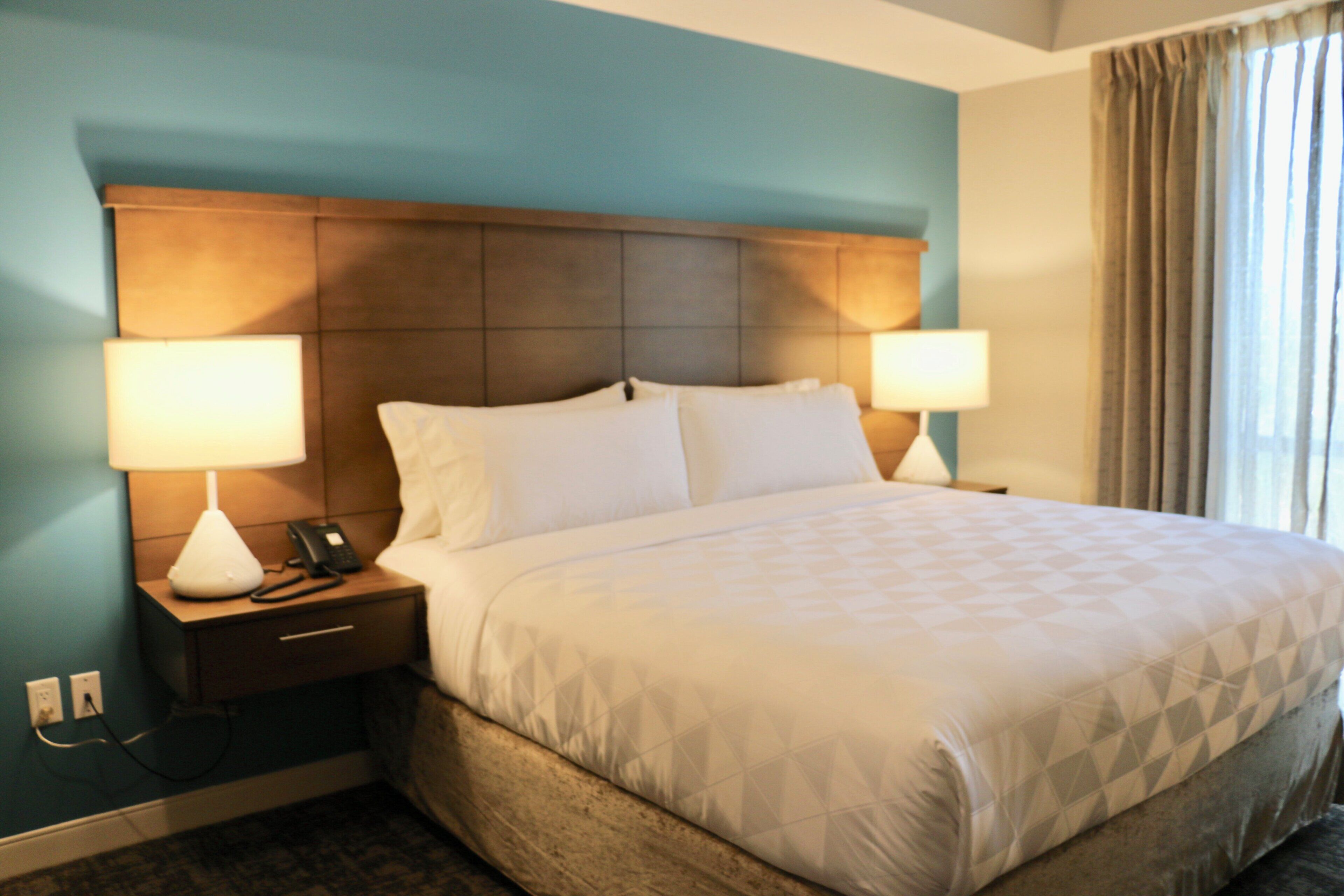 A hotel room with a large bed, two bedside lamps, a telephone, and a nightstand.