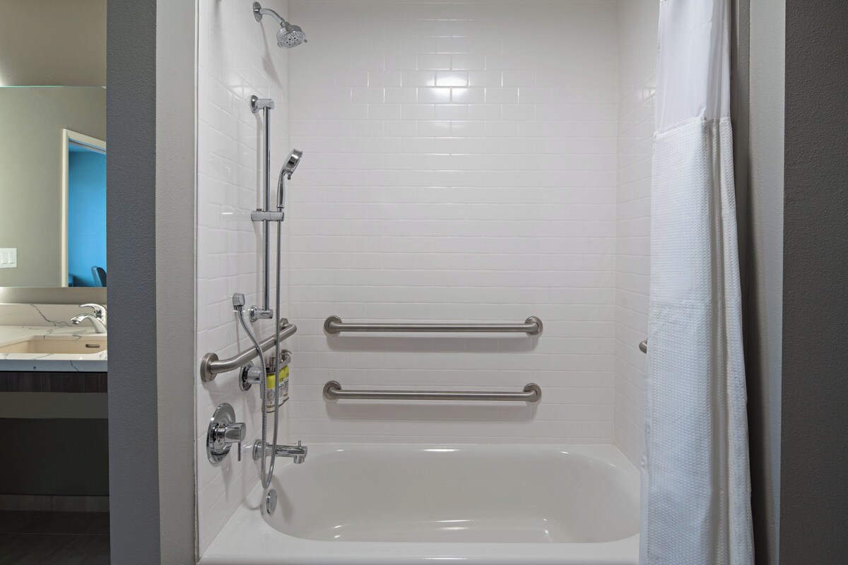 Un baño con una bañera blanca, barras de apoyo y cabezal de ducha.