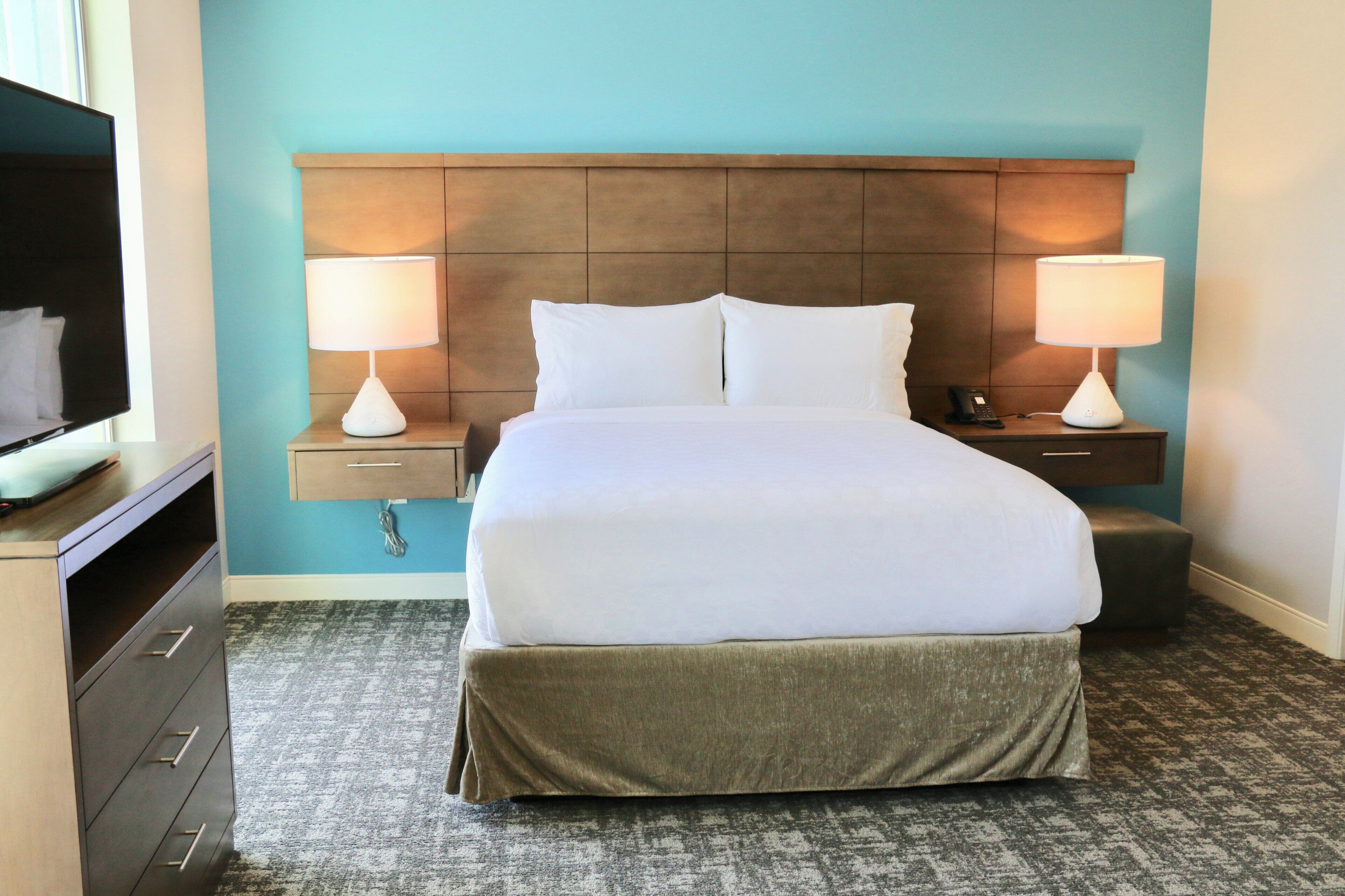 A hotel room with a bed, two bedside tables, a TV, a desk, and a carpeted floor.