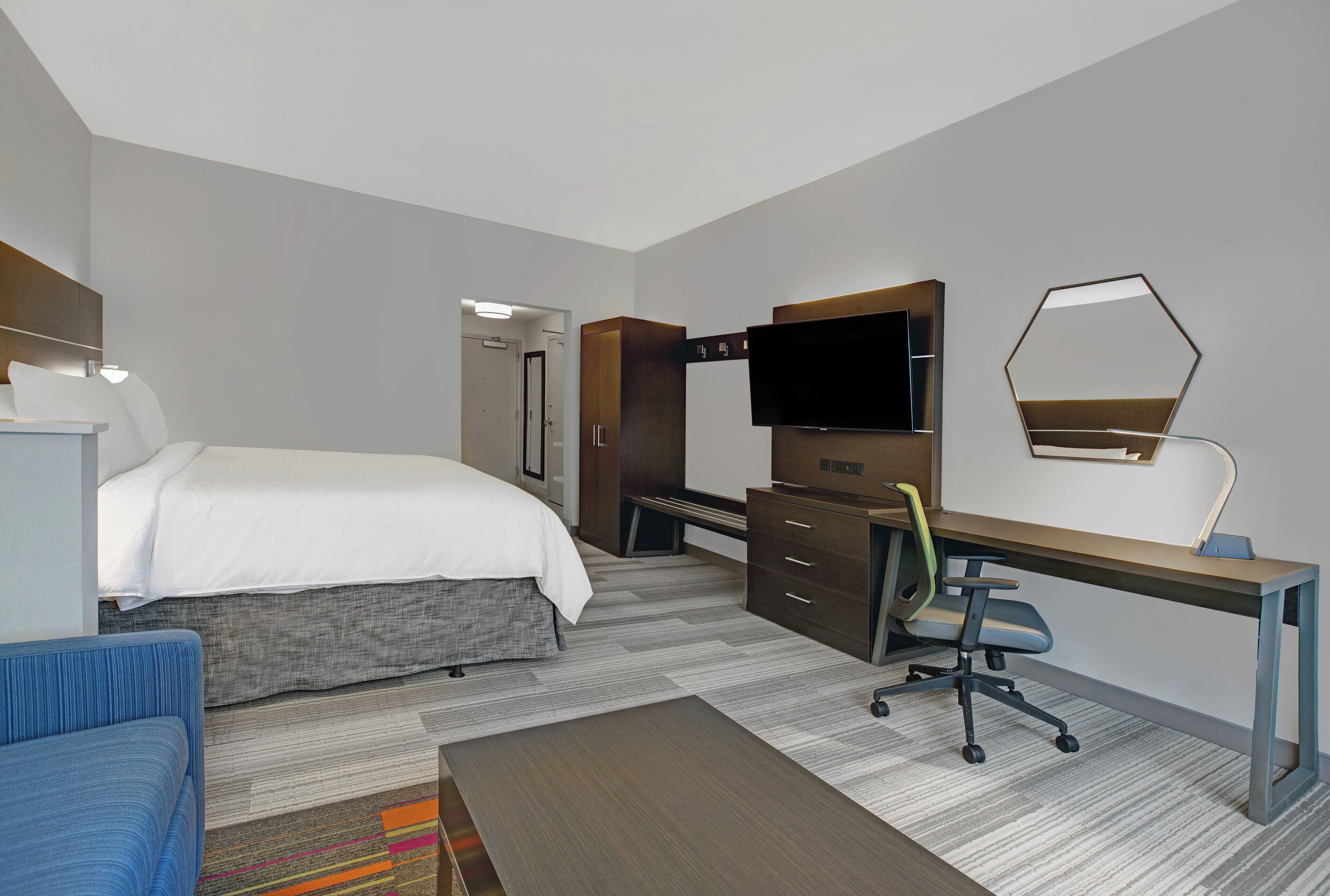 A hotel room with a bed, a desk, a chair, a TV, and a mirror.