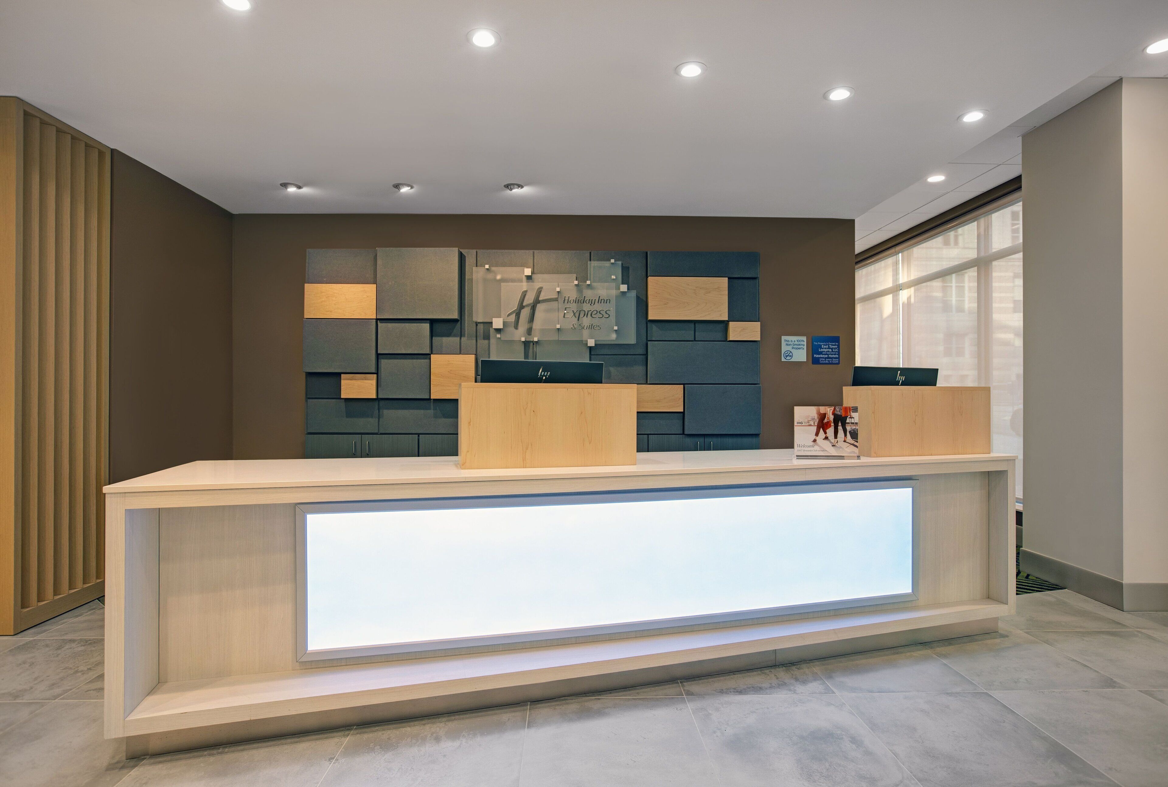 A hotel reception desk with a modern design, featuring a light wood finish and a glass display case.