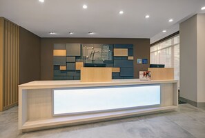 A hotel reception desk with a modern design, featuring a light wood finish and a glass display case. - Holiday Inn Express Milwaukee Downtown by IHG (Milwaukee)