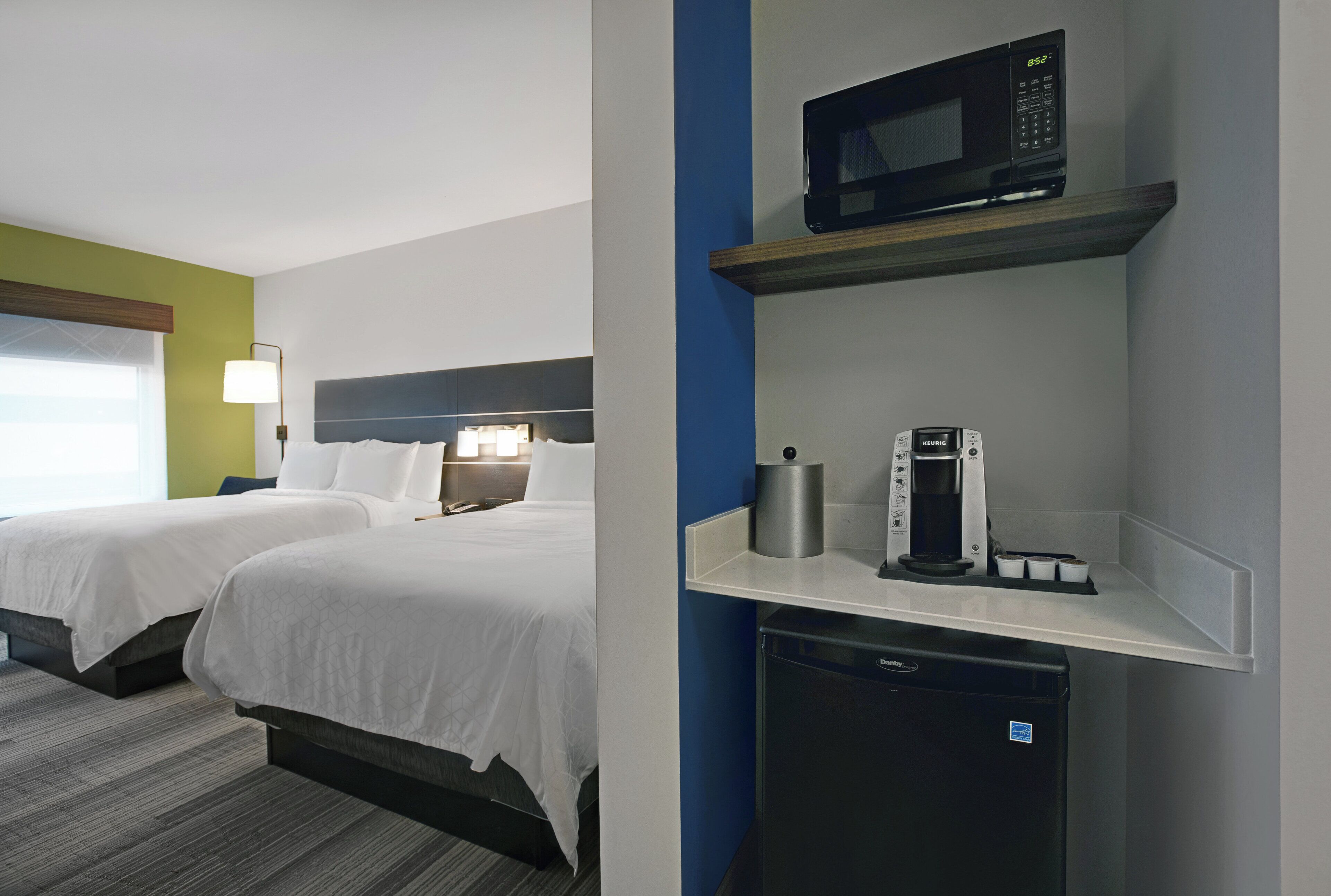 A hotel room with two beds, a microwave, a coffee maker, and a small refrigerator.