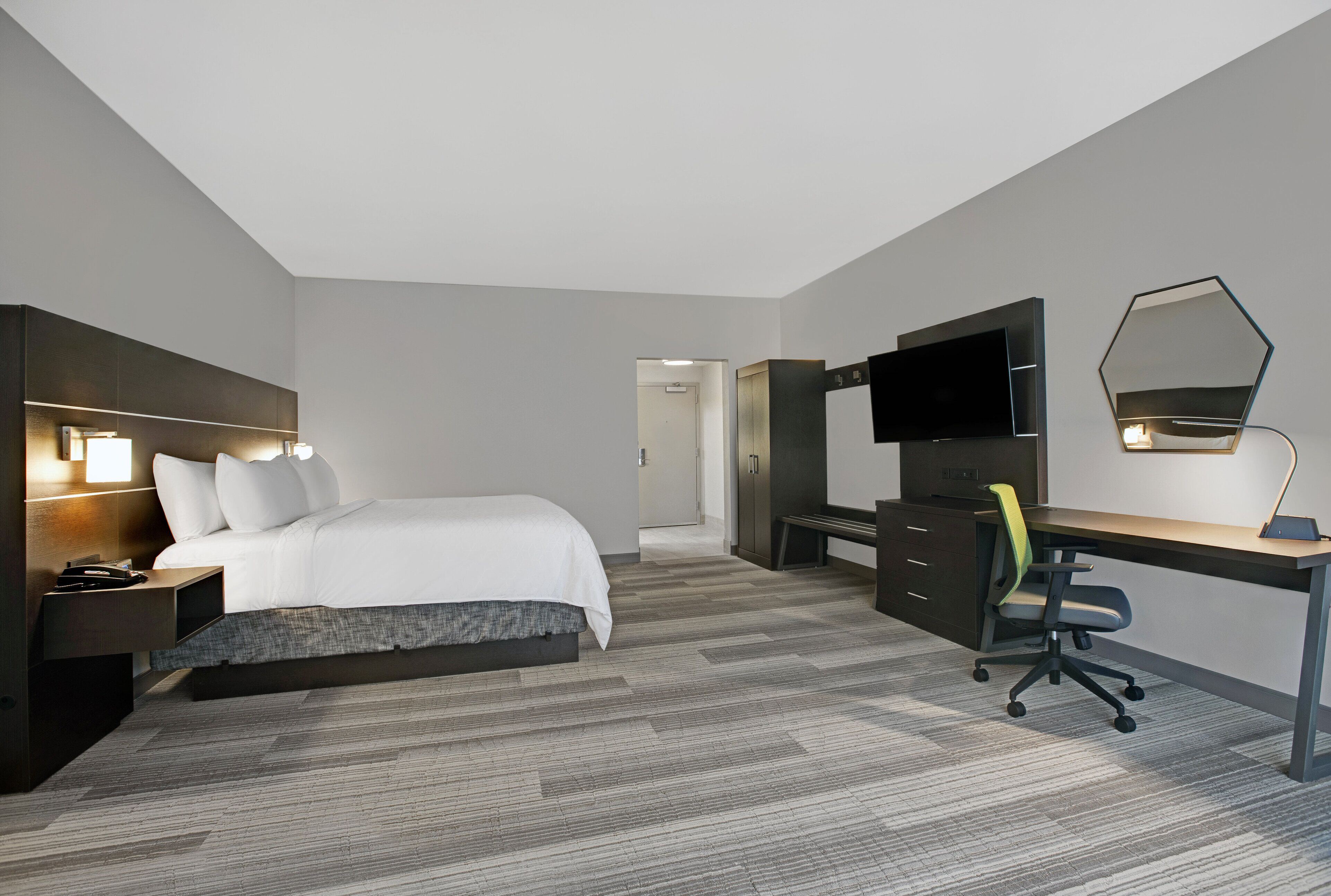 Une chambre d’hôtel avec un lit, un bureau, une télévision et un miroir.
