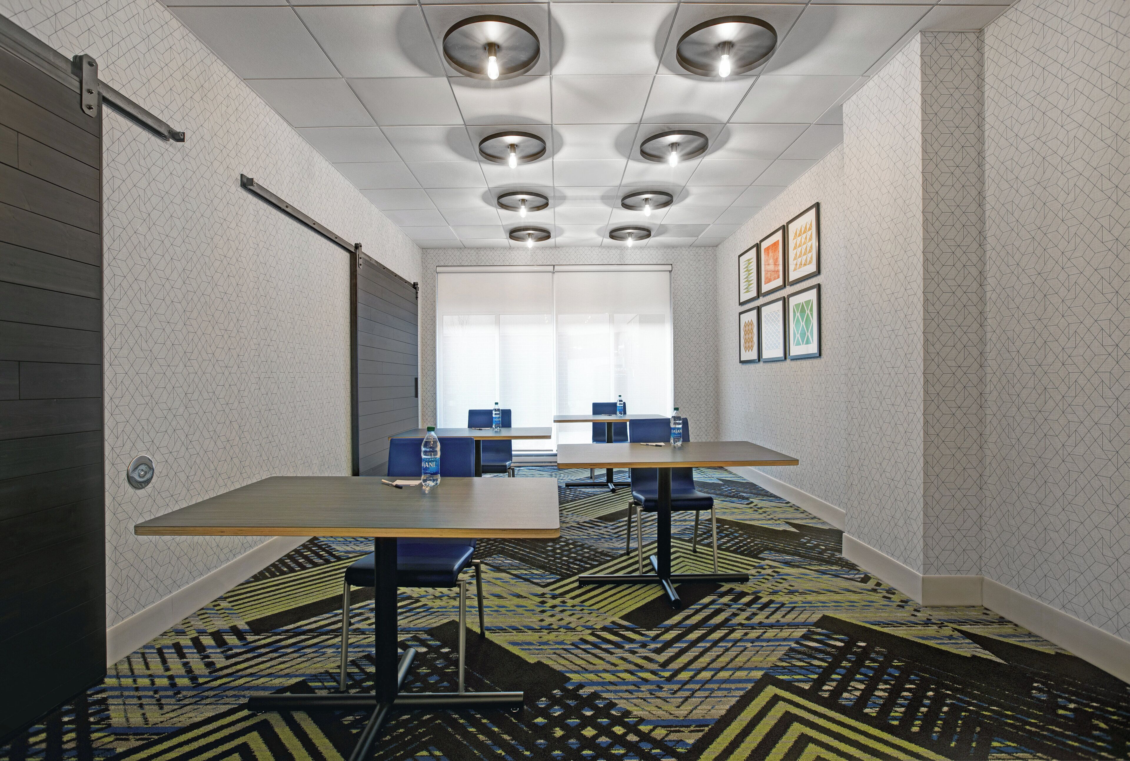 Una sala de conferencias con alfombra de estampado geométrico, una mesa de madera y sillas azules.