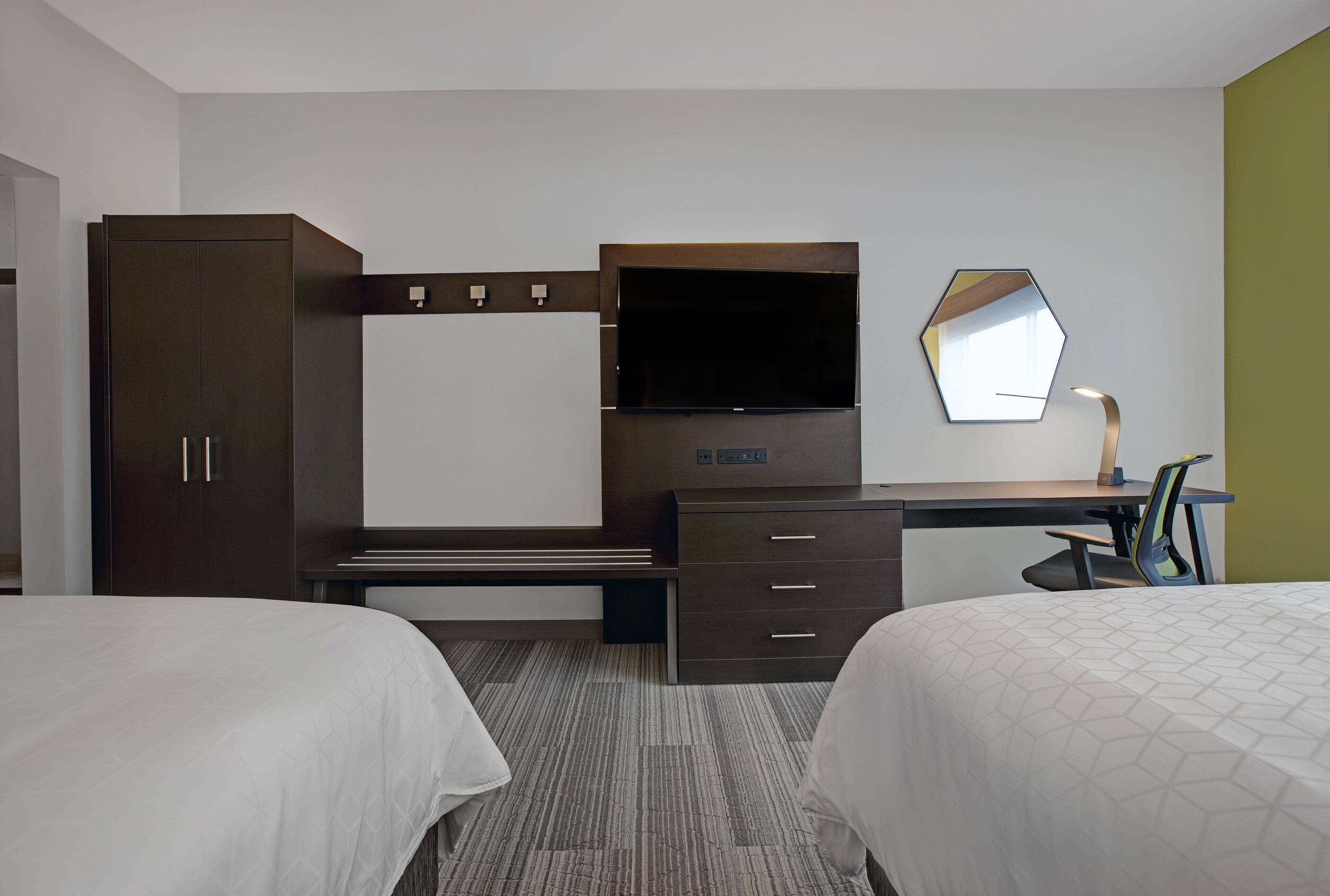 Une chambre d’hôtel avec deux lits, un bureau doté d’un téléviseur à écran plat, une armoire et un miroir.