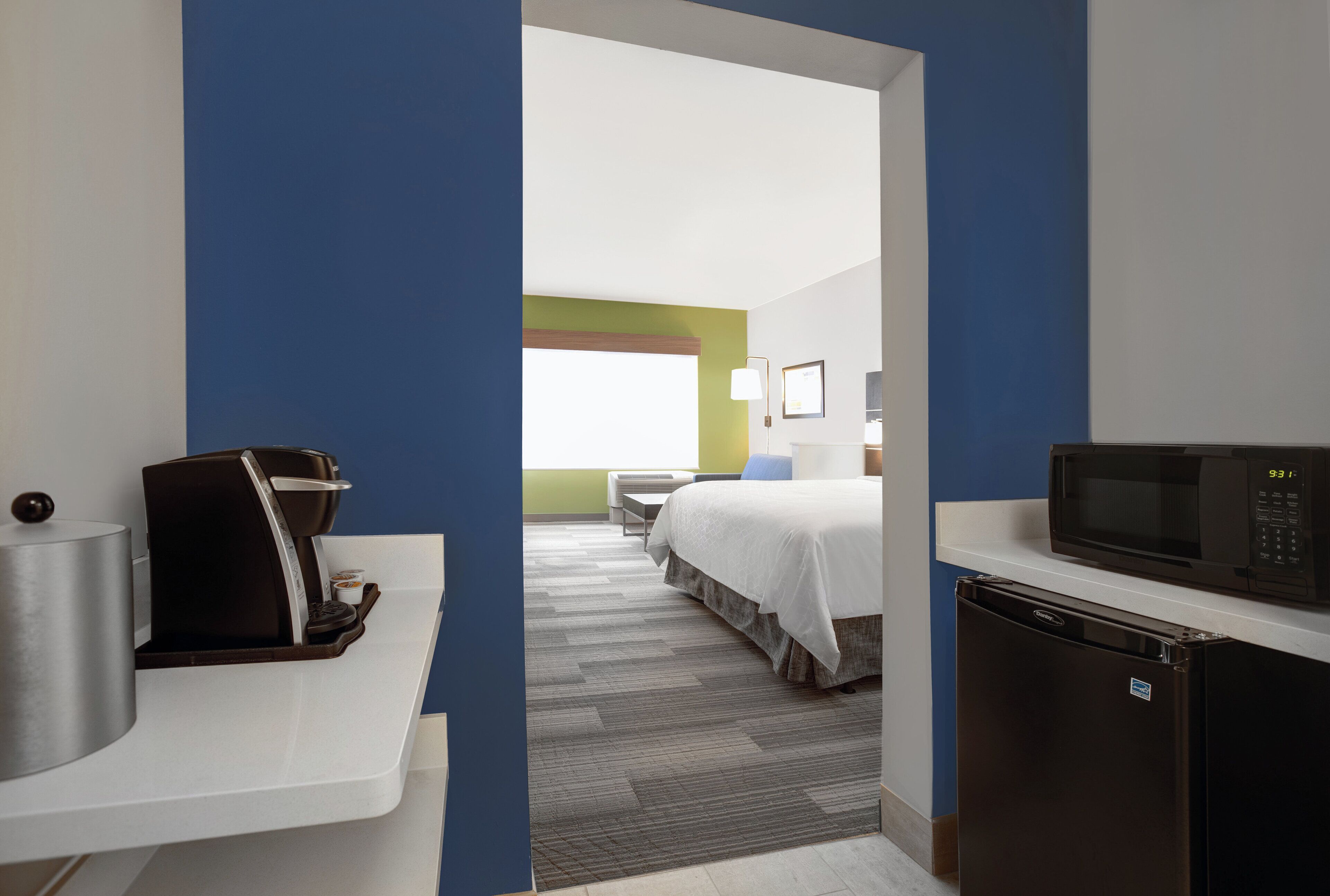 A hotel room with a kitchenette, a bed, a desk, and a microwave.