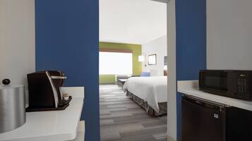 A hotel room with a kitchenette, a bed, a desk, and a microwave.