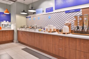 Una barra de desayuno moderna con diversas opciones de cereales, una estación de café y un cartel que indica el horario del desayuno.