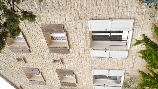 Un bâtiment doté de nombreuses fenêtres et de balcons, de murs en pierre et de quelques éléments de végétation.