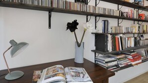 Une pièce avec un bureau en bois, une lampe, un vase rempli de fleurs et des étagères remplies de livres et de CD.