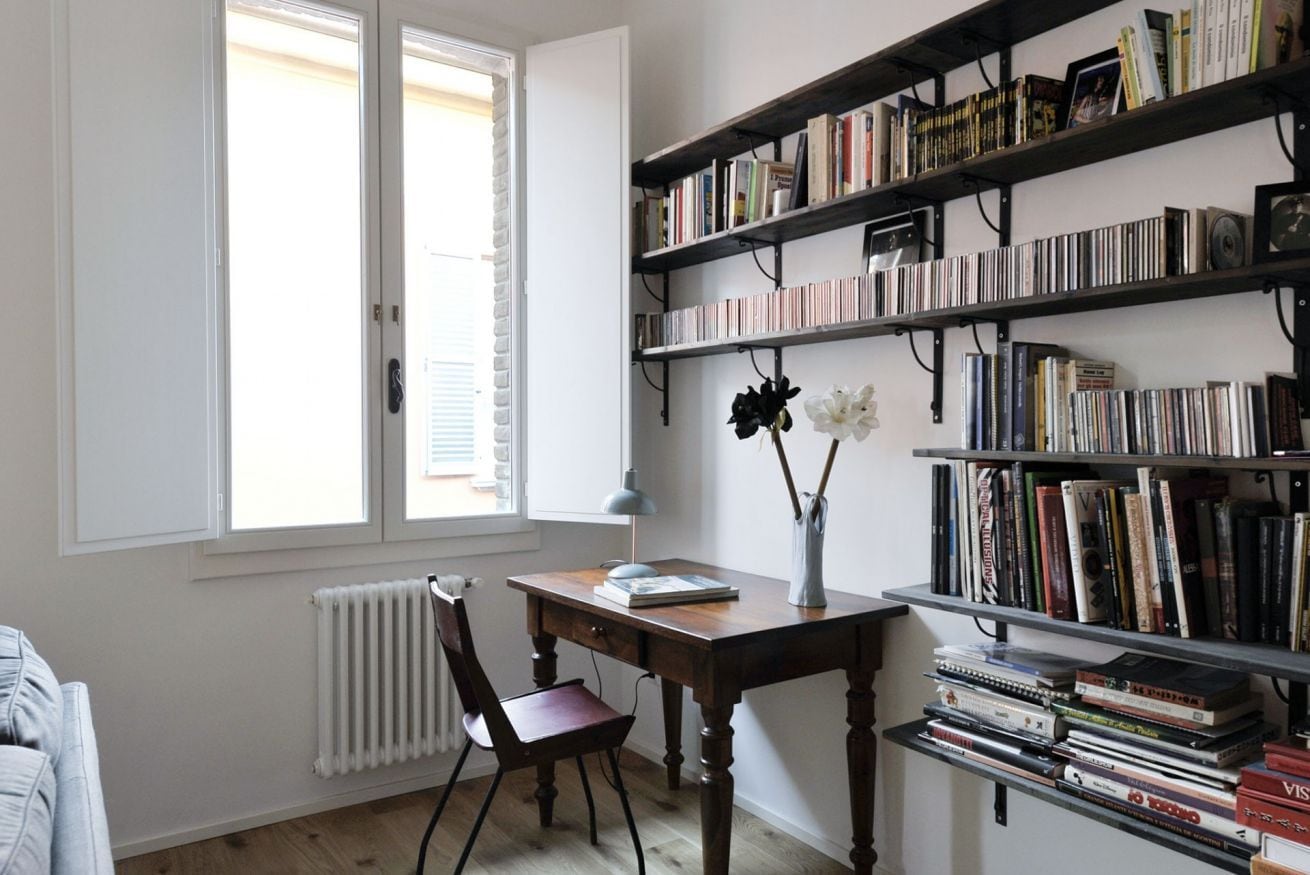 A study room with a wooden desk, a chair, a bookshelf, and a radiator.