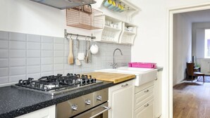 Une cuisine moderne dotée d’une cuisinière à gaz, d’un plan de travail en bois, de meubles blancs et d’un bac de rangement rose.