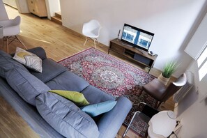 A modern living room with a grey sofa, a red and white patterned rug, a television on a wooden stand, and a potted plant. - UR-NEST Testoni, Elegant and quaint two bedroom (Bologna)