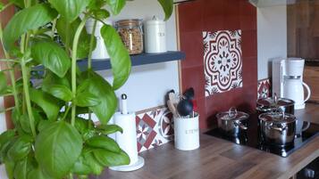 A kitchen with a wooden countertop, a potted basil plant, a coffee maker, and stainless steel pots.