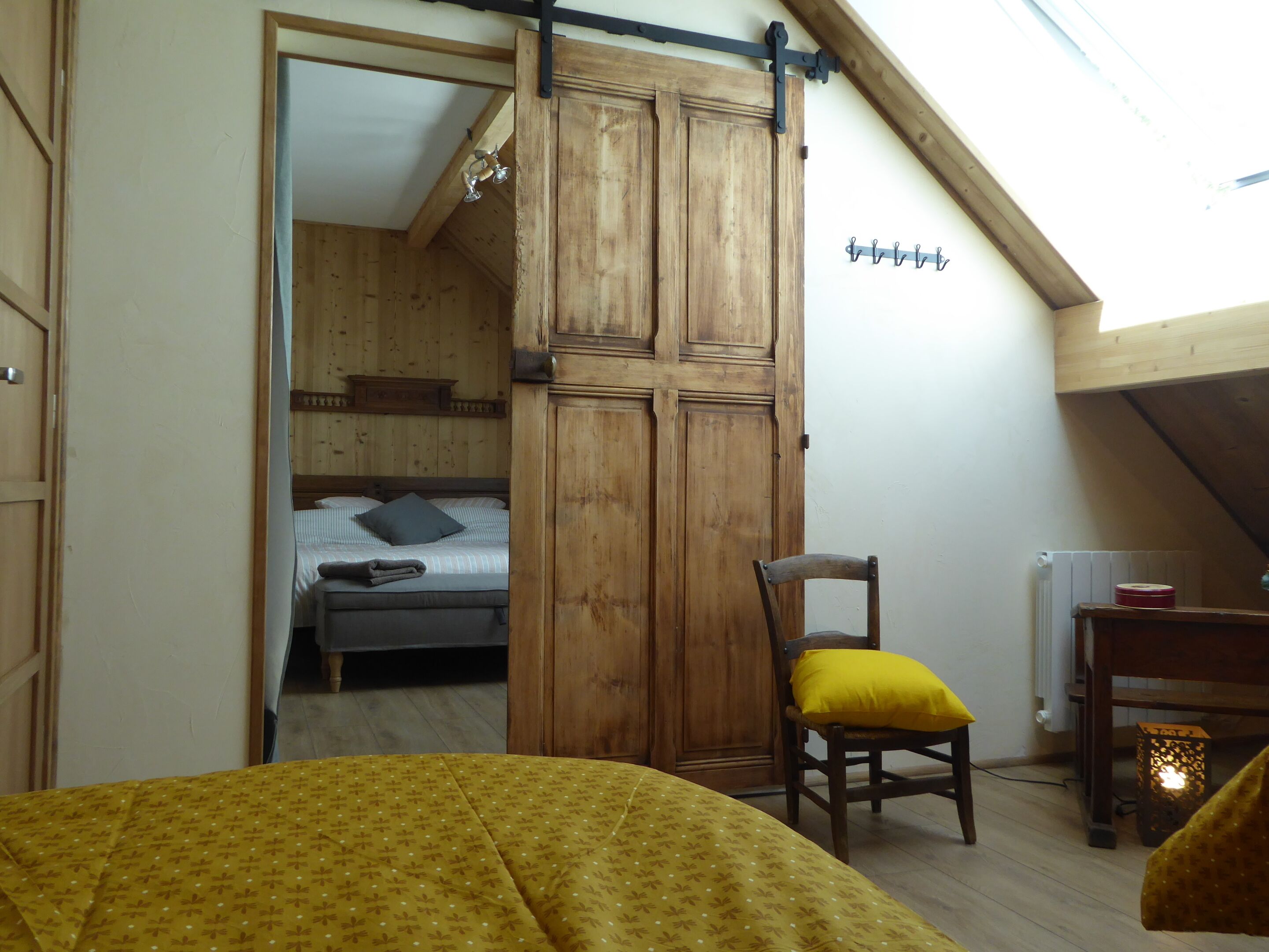 Een kamer met een bed, een houten garderobe, een stoel met een geel kussen, een radiator en een hanglamp.