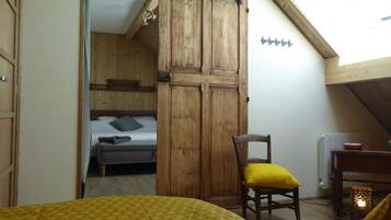 Een kamer met een bed, een houten garderobe, een stoel met een geel kussen, een radiator en een hanglamp.