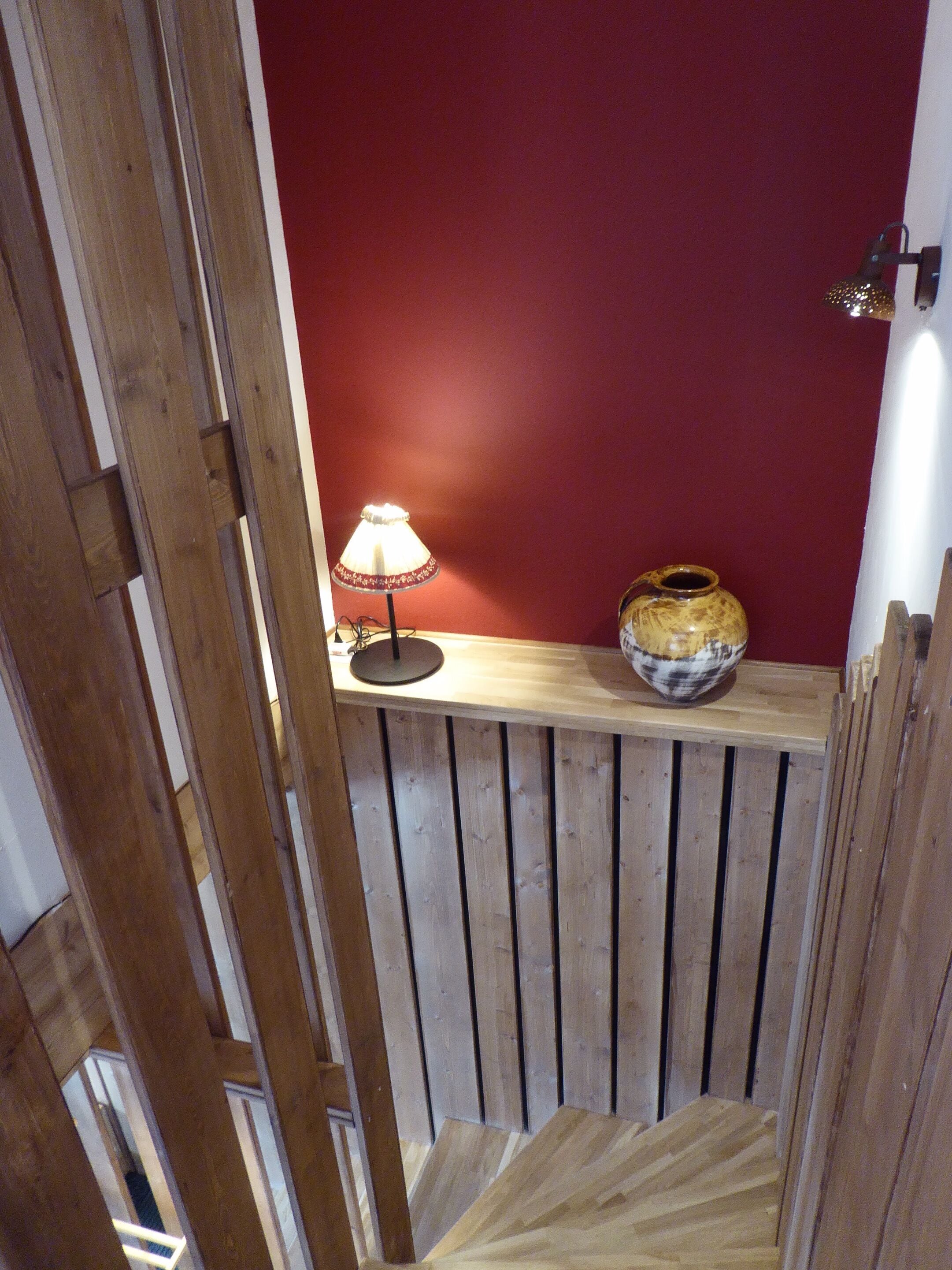 A wooden staircase with a red wall, a lamp, and a decorative bowl on the landing.